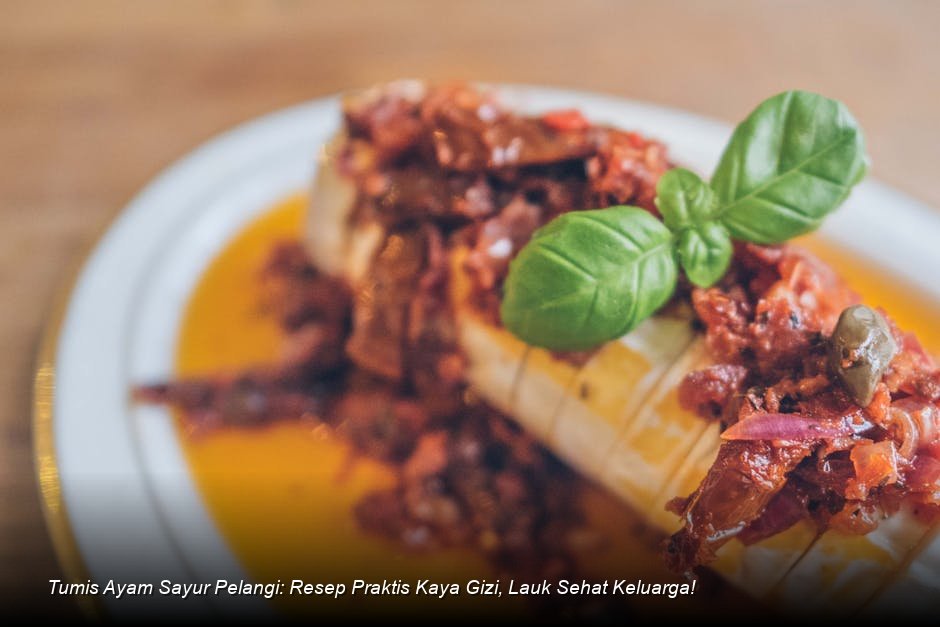 Semangkuk penuh Tumis Ayam Sayur Pelangi yang mengkilap, menampilkan potongan ayam, brokoli hijau cerah, dan irisan paprika merah, disajikan di atas piring keramik putih.